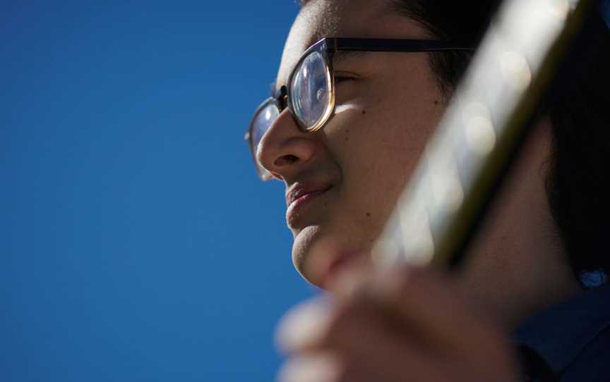 Young person with guitar against bright blue sky