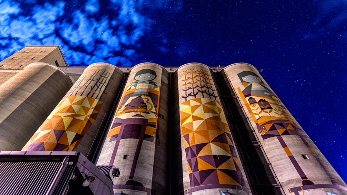 Two stylised and colourful figures painted across four enormous grain storage silos