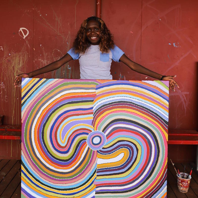 Aboriginal Warlayirti Artist holding her colourful Aboriginal dot painting