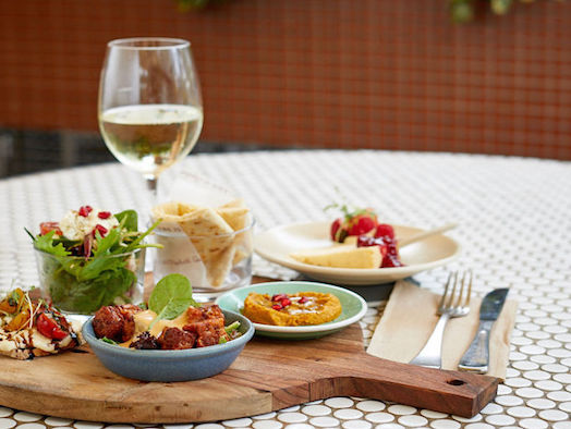 A glass of white wine sits beside a platter of tapas